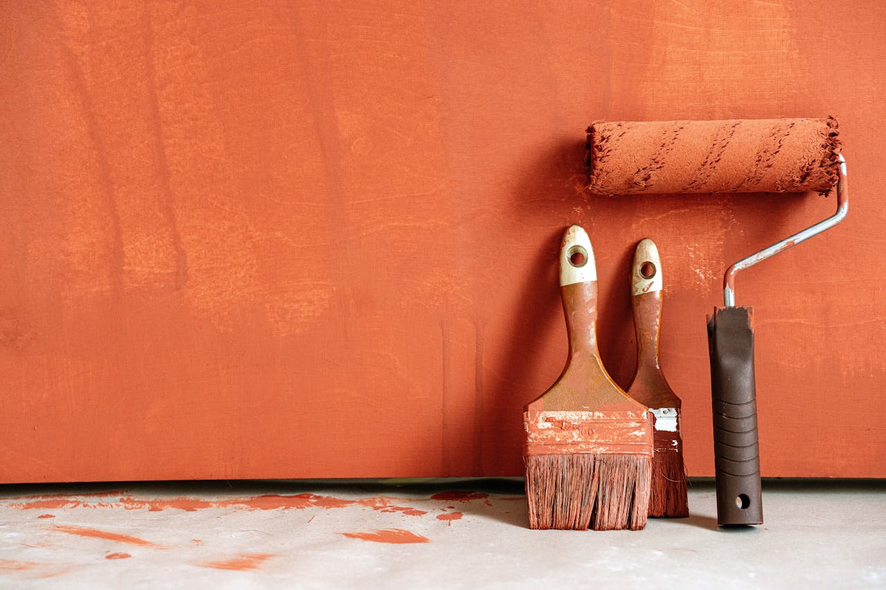 creative-03 Close-up of paint rollers and brushes with orange paint against a painted wall.