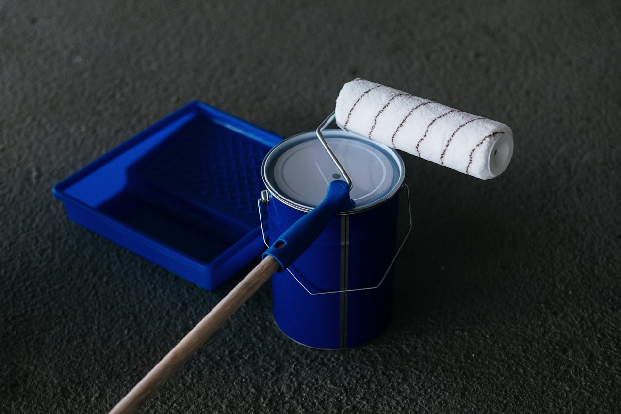 Close-up of a paint can, roller, and tray on a textured floor, perfect for DIY projects.
